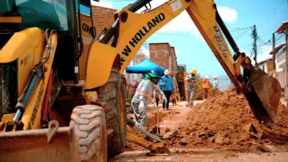 Máquina escavadeira e trabalhadores durante obras de infraestrutura de saneamento.