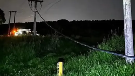 Postes e cabos de rede elétrica caídos em área de vegetação à noite