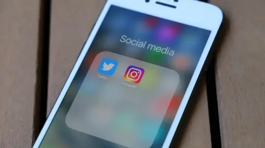 Imagem ilustrativa de celular com aplicativos de redes sociais sobre uma superfície de madeira