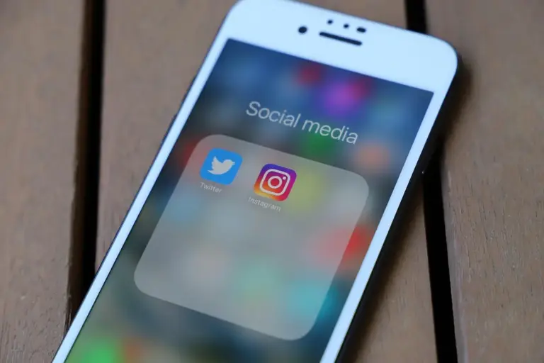 Imagem ilustrativa de celular com aplicativos de redes sociais sobre uma superfície de madeira