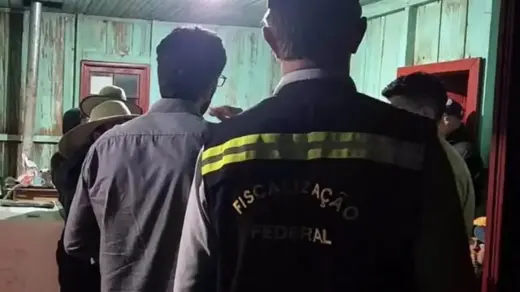 Agentes de fiscalização durante vistoria no interior de um alojamento de madeira